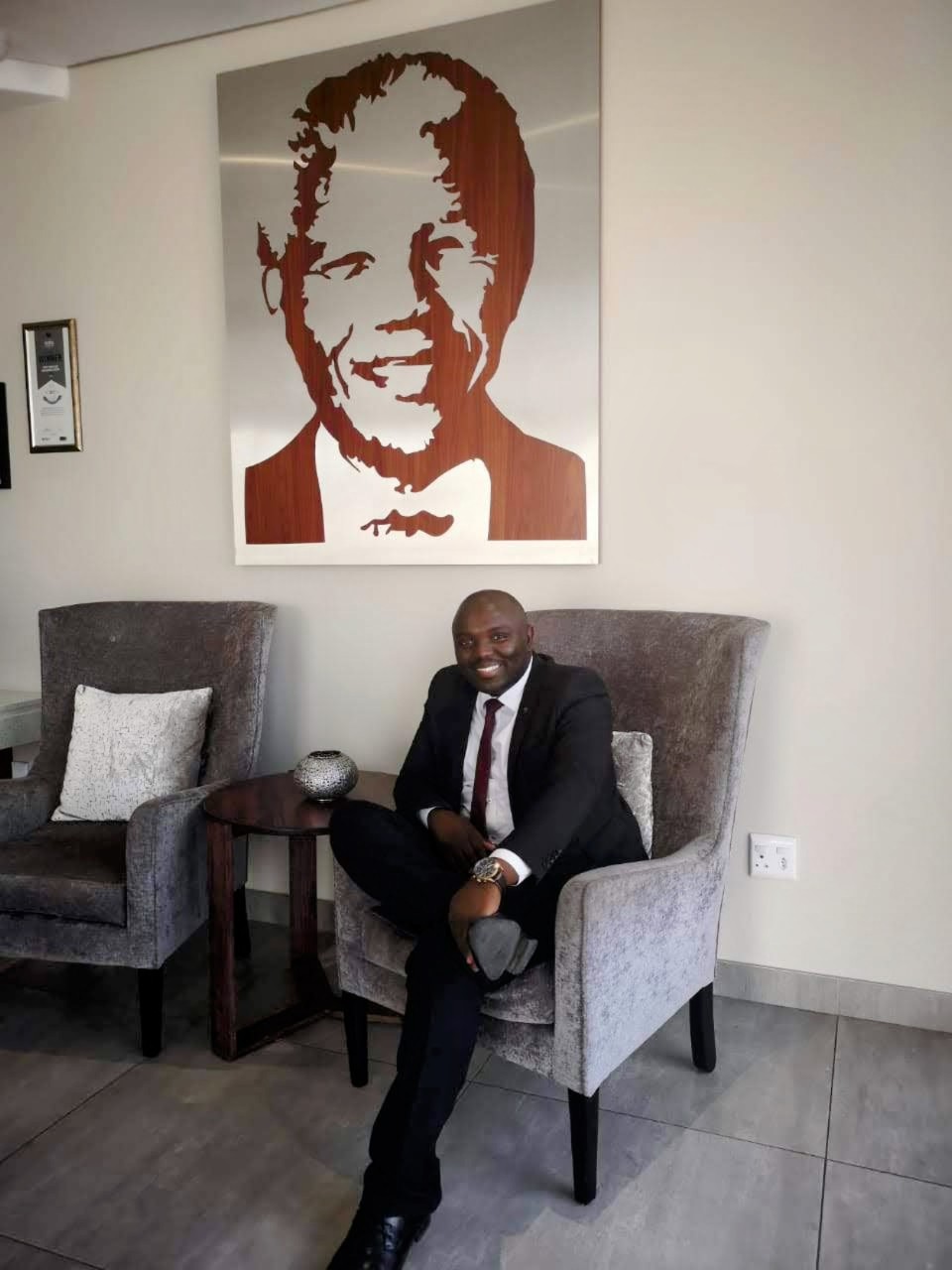 Senzo Mkhize, Credico South Africa's 2024 Employee of the Year, sits in an armchair under a portrait of Nelson Mandela.