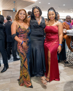 Three smiling attendees in formal gowns pose for a photo before the South Africa Awards Gala in March 2025