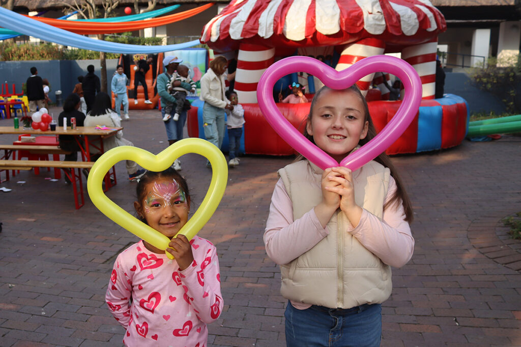 two girls pose with their heart-shaped balloons at Credico South Africa's 2025 Christmas in July
