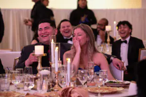 Seen through a glittering gold centerpiece with candles, attendees laugh and smile at one of the speeches during the 2026 Limitless Kickoff Gala