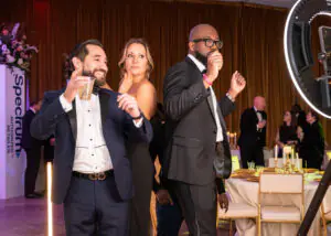 Three attendees stand closely together on a pedestal as a 360-degree camera swings around them at the 2026 Limitless Kickoff Gala